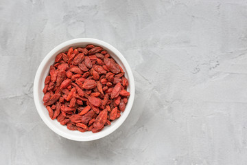 Dried goji berries in a porcelain bowl on a gray background