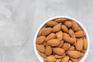 Raw almonds in a porcelain bowl on a gray background