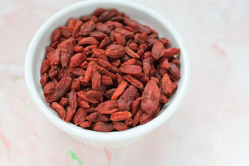 Dried goji berries in a porcelain bowl on a pink background