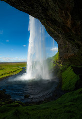 Seljalandsfoss a majestic and powrful Icelandic waterfall in Iceland. The cascading water spills along the rustic cliffside meadow full of lush green grass and jet blue skies.