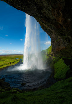 Seljalandsfoss a majestic and powrful Icelandic waterfall in Iceland. The cascading water spills along the rustic cliffside meadow full of lush green grass and jet blue skies. © Thorin Wolfheart