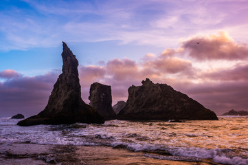 Epic colors at the rugged coast where the sea stacks stand in the ocean. The tall structures give a dark texture to the ocean and sandy beach. Amazing colors fill the sky as the sun sets on horizon