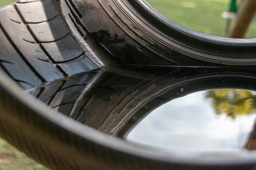 A close up view of the reflection of the trees in water that has been sitting in a black rudder swing hanging on a jungle gym