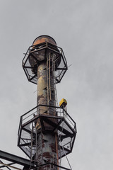 Industrial smokestack with ladders and walkways against a gray sky, vertical aspect