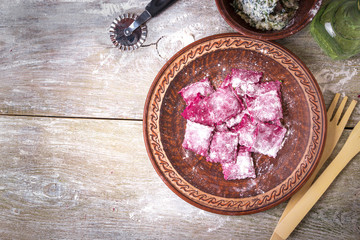 Obraz na płótnie Canvas Homemade raw pink beetroot pasta ravioli with cheese and parsley in a plate, on wooden rustic background