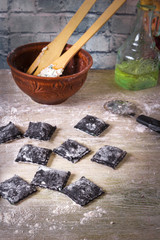 Homemade raw black cuttlefish ink ravioli with ricotta cheese and parsley on a wooden rustic background