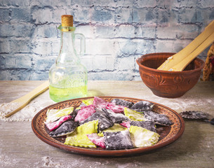 Three color homemade raw pink beetroot, green spinach and black cuttlefish ink pasta ravioli with cheese and parsley in a plate, on wooden rustic background