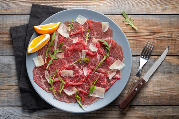Marbled beef carpaccio with arugula, lemon and parmesan cheese on wooden table. Top view, flat lay