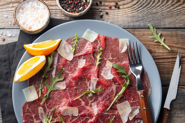 Marbled beef carpaccio with arugula, lemon and parmesan cheese on wooden table. Top view, flat lay