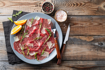Marbled beef carpaccio with arugula, lemon and parmesan cheese on wooden table. . Top view, flat lay with copy space