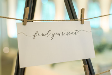 White "find your seat" wedding reception sign hung with clotes pins