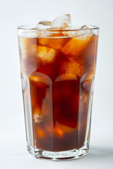 Ice coffee in a tall glass with cream poured over and coffee beans. Cold summer drink on a light background