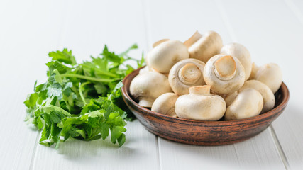 Mushrooms in a bowl with parsley leaves on a white wooden table. Vegetarian cuisine.