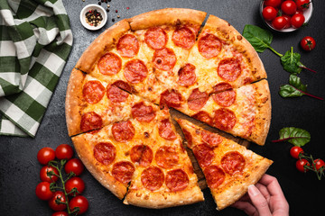 Pepperoni pizza on a black concrete background. Hand picking slice of pepperoni pizza. Table top...