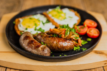 Traditional potato pancakes with fried eggs, mushrooms, sausages and tomatoes served on a hot frying pan.