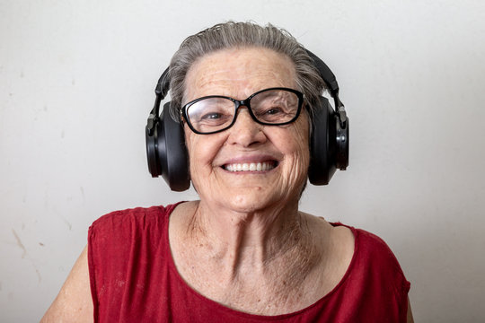 Lifestyle And People Concept: Funny Old Lady Listening Music And Dancing On White Background. Elderly Woman Wearing Glasses Dancing To Music Listening On His Headphones.