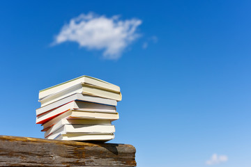Books stacked on a wooden bench under blue sky
