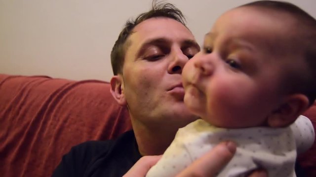 Father is trying to teach his six months old baby boy to say mama. Baby is puting hand on his mouth to stap speaking . funny baby
