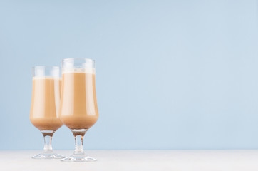 Refreshment cold coffee drink in two goblets with cream and foam in modern light pastel blue interior on white wood table, copy space.