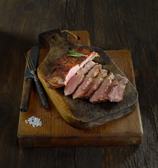 Sliced grilled  barbecue steak   on cutting board on dark wooden background