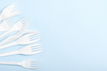 Plastic white disposable forks and knives on a blue background. Concept plastic dishes, fast food, plastic pollution. Copy space, top view, flat lay.