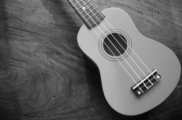 A ukulele on wooden background black and white shade.On some family holidays Use the ukulele to sing and sing as a common activity.Some people call Ukelele.