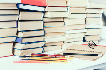 Stack of old books, textbook, notebook, glasses and pencils on white table in office background for education concept.