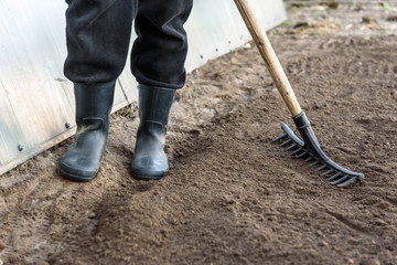 Farmer working in garden with rake leveling ground. Preparation of ground for planting.