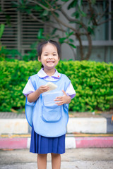 Portrait of happy little girl in Thai school uniform standing and eating bread in the morning, ready back to school