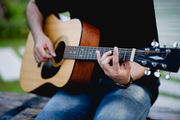 Picture of a guitarist, a young man playing a guitar while sitting in a natural garden,music concept