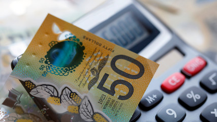 Australian fifty dollar bill over a calculator. The new 2019 issue is designed to deter counterfeiting, the note is polymer and water resistant with a clear holographic strip