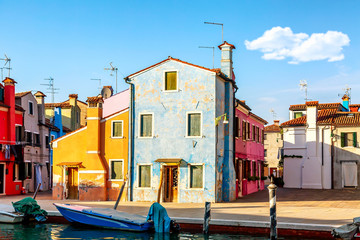 Colorful houses in Burano near Venice, Italy with boats and beautiful blue sky in summer. Famous tourist attraction in Venice.