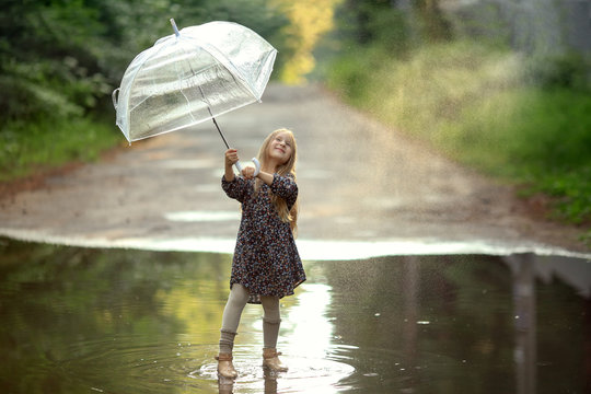 girl with long hair and with an umbrella in a beautiful dress and shoes standing under the spray of water