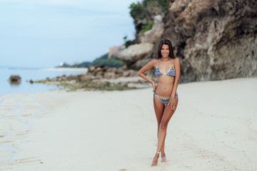 Obraz premium Young smiling sexy girl with perfect body in colored swimwear resting on white sand beach