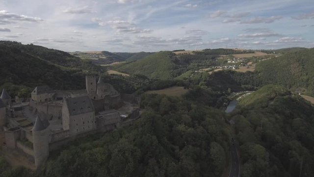 Passing above the forest right next Bourscheid castle in Luxembourg. Showing the mountains, forests, village, river, bridge and a traing passing by. Sunny weather with clouds.