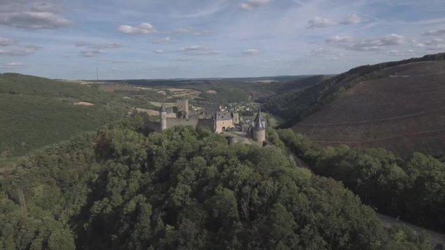 Drawing away from Bourscheid castle in Luxembourg. Showing the surrounding mountains and village in back, fading above the forests. Sunny weather with clouds.