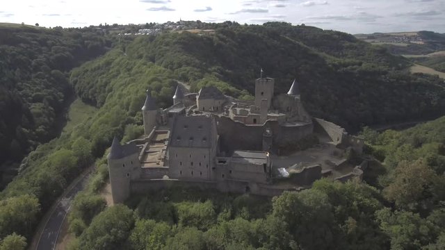 Drawing away above Bourscheid castle in Luxembourg. Showing the surrounding mountains, forests and village in the back. Sunny weather with clouds.
