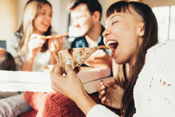 Group of friends at home party eating pizza together. Bright sunny apartment