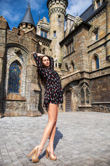 Fototapeta na wymiar Full-length portrait young beautiful girl in summer dress posing against the backdrop of an old castle in the Gothic style