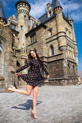 Fototapeta na wymiar Full-length portrait young beautiful girl in summer dress posing against the backdrop of an old castle in the Gothic style
