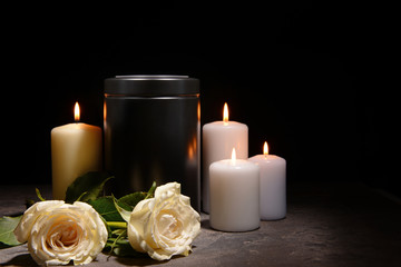 Obraz na płótnie Canvas Mortuary urn, burning candles and flowers on table against dark background