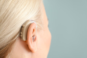 Mature woman with hearing aid on color background, closeup