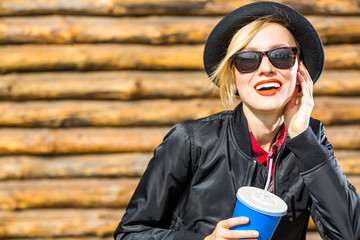 Smiling fashionable blonde drinking cola outdoors on wooden background