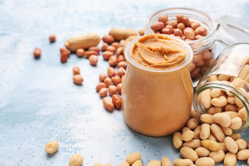Jars with tasty peanut butter and nuts on color background
