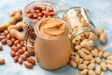 Jars with tasty peanut butter and nuts on color background
