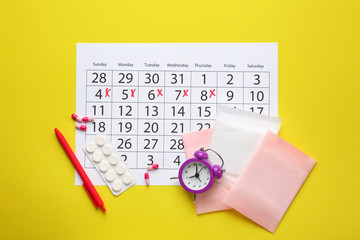 Menstrual calendar with pads, pills and alarm clock on color background