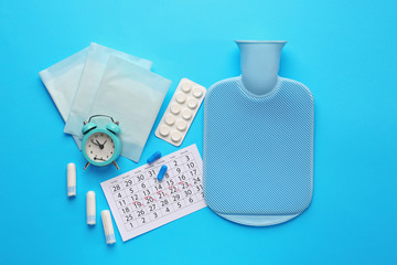 Menstrual calendar with feminine products, alarm clock, water bag and pills on color background