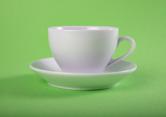 White mug and saucer on a green background.