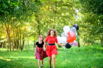 Fototapeta premium Two girls sit on the grass in the evening park with air balloons, happy kids concept