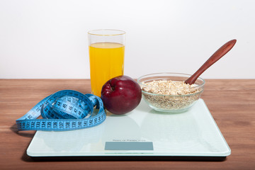 The concept of healthy diet, fitness and weight loss. Scales, measure tape, oatmeal, apple, a glass of juice on the table.